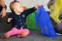 Kleinkind streckt sich nach einem aufgehängten farbigen Tuch