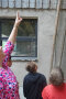 2 Kinder schauen auf Bretterverkleidung eines Gebäudes, Erwachsene zeigt mit Finger darauf