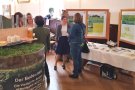 Fass mit Poster "Der Boden lebt", daneben Personen an Infostand