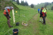 Personen stehen auf Wiese und errichten Zaun