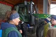 Frau steht mit Kindern vor grünem Traktor