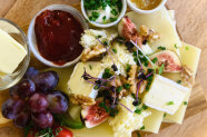 Käse, Trauben, Nüsse, Sprossen, Kräuteraufstrich, Butter und Marmelade auf einem Brett