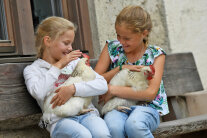 Zwei Mädchen halten Hühner in den Armen